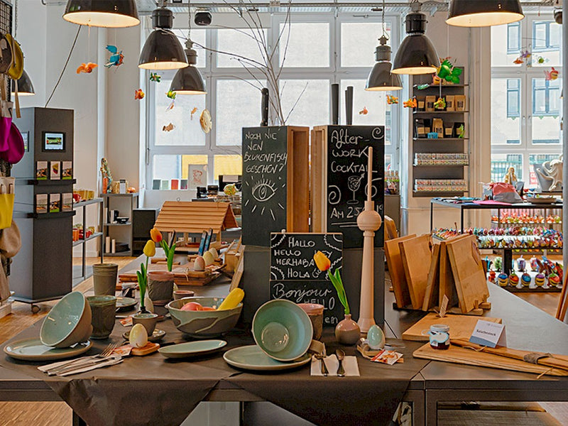 Auf dem Bild sieht man ein Teil des Blumenfisch Laden. Im Vordergrund sieht man einen Tisch, welcher mit vielen bunten Handwerksprodukten bestückt ist.