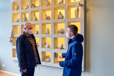 Blumenfisch-Mitarbeiter Ronald Bluhm und Special Olympics Praktikant Julian Stegemann. Im Hintergrund sind Kunstwerke der Mitarbeiter in einem Regal sichtbar.