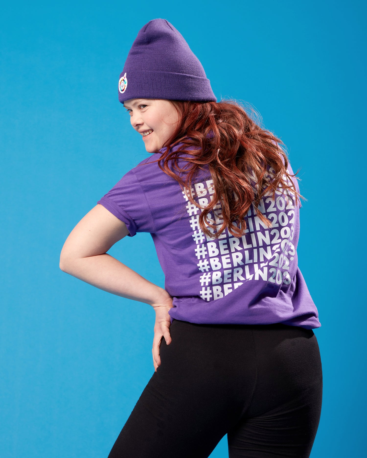 Mädchen steht mit dem Rücken zur Kamera. Sie trägt ein violettes T-Shirt mit kleinem 	Weltspiele Logo auf der Brust und einer violetten Mütze.
