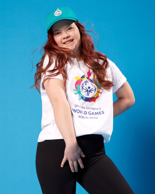 Mädchen trägt weißes T-Shirt mit großem Weltspiele Logo vorn und ein petrolfarbenes Cap.
