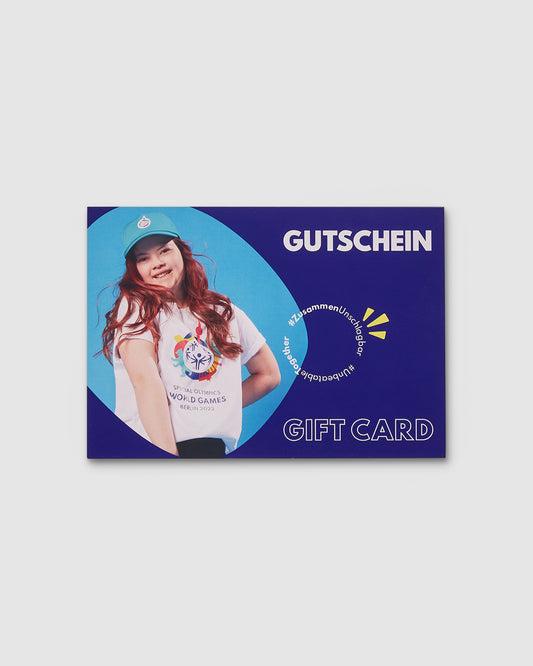 Auf der blauen Gutscheinkarte ist ein Bild des Models Julie, die ein T-Shirt und eine Mütze mit Weltspiele Logo trägt. Das Wort Gutschein und das Motto #ZusammenUnschlagbar stehen jeweils in weiß auf Deutsch und auf Englisch auf der Karte. 