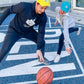 Eine Frau und ein Mann spielen Basketball, der Mann trägt einen schwarzen Hoodie mit Weltspiele Logo und die Frau trägt einen grauen Hoodie mit Weltspiele Logo 