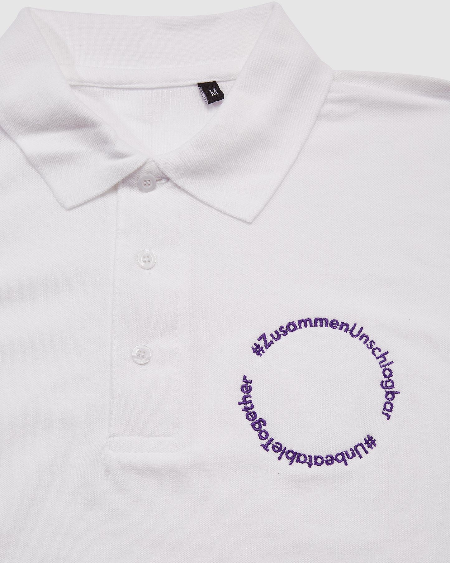 Nahaufnahme weißes Polo-Shirt, mit Schriftzug '#ZusammenUnschlagbar' auf der Brust