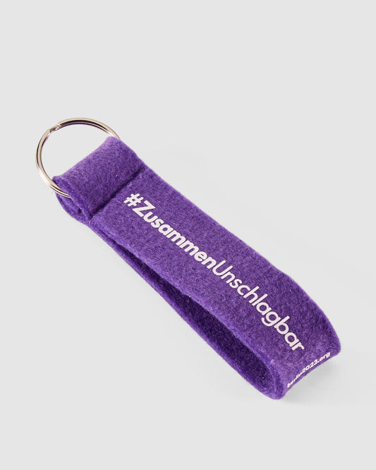 Schlüsselanhänger in violett mit #ZusammenUnschlagbar Schriftzug in weiß vorn
