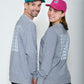 Mann und Mädchen stehen nebeneinander und schauen in die Kamera. Der Mann trägt ein graues Sweatshirt und eine Cap in Petrol mit Logo. Das Mädchen trägt ein graues Sweatshirt und pinke Cap mit Logo. 