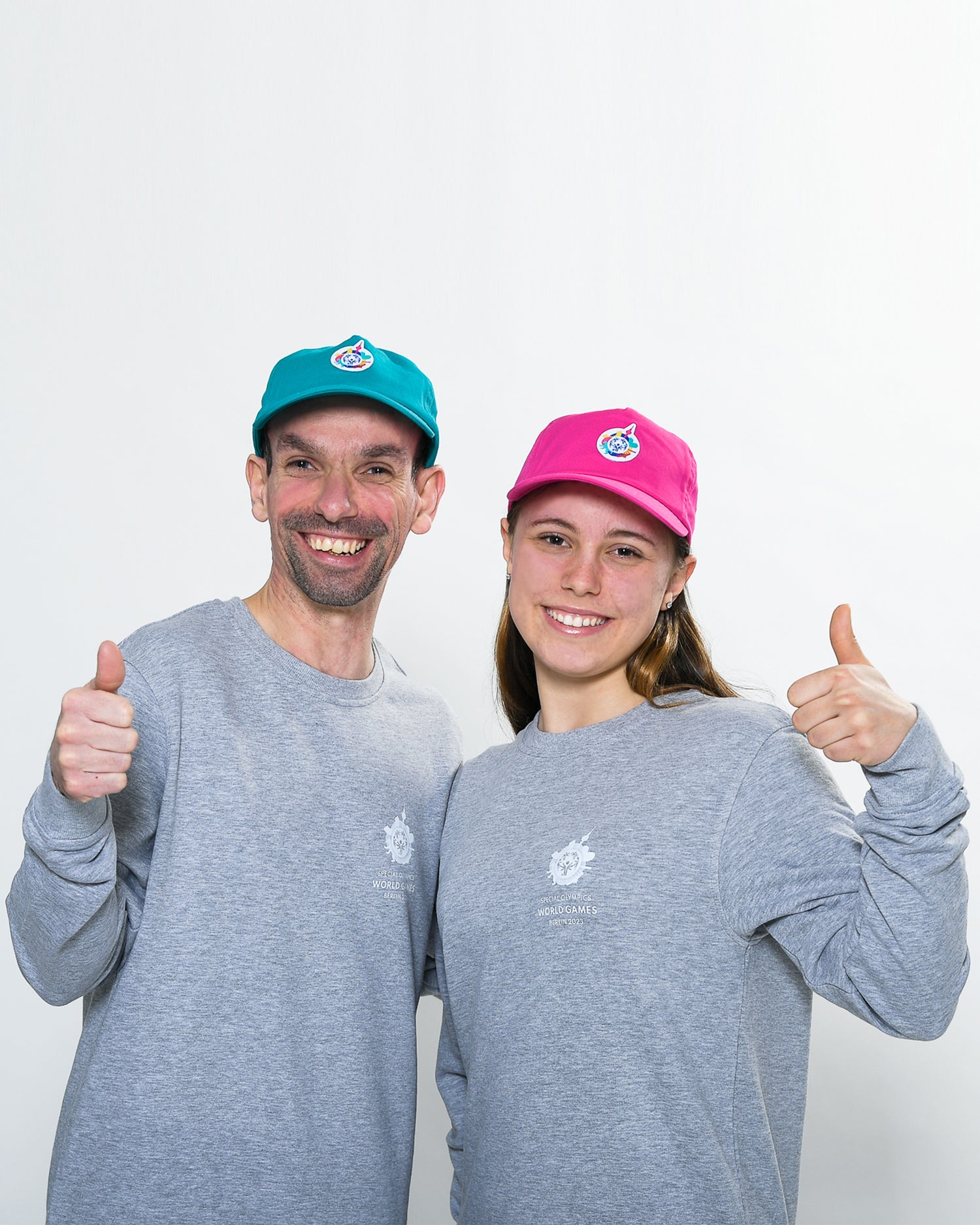 Mann und Mädchen stehen nebeneinander. Beide tragen graue Sweatshirts mit 	einem kleinen Weltspiele Logo auf der Brust.